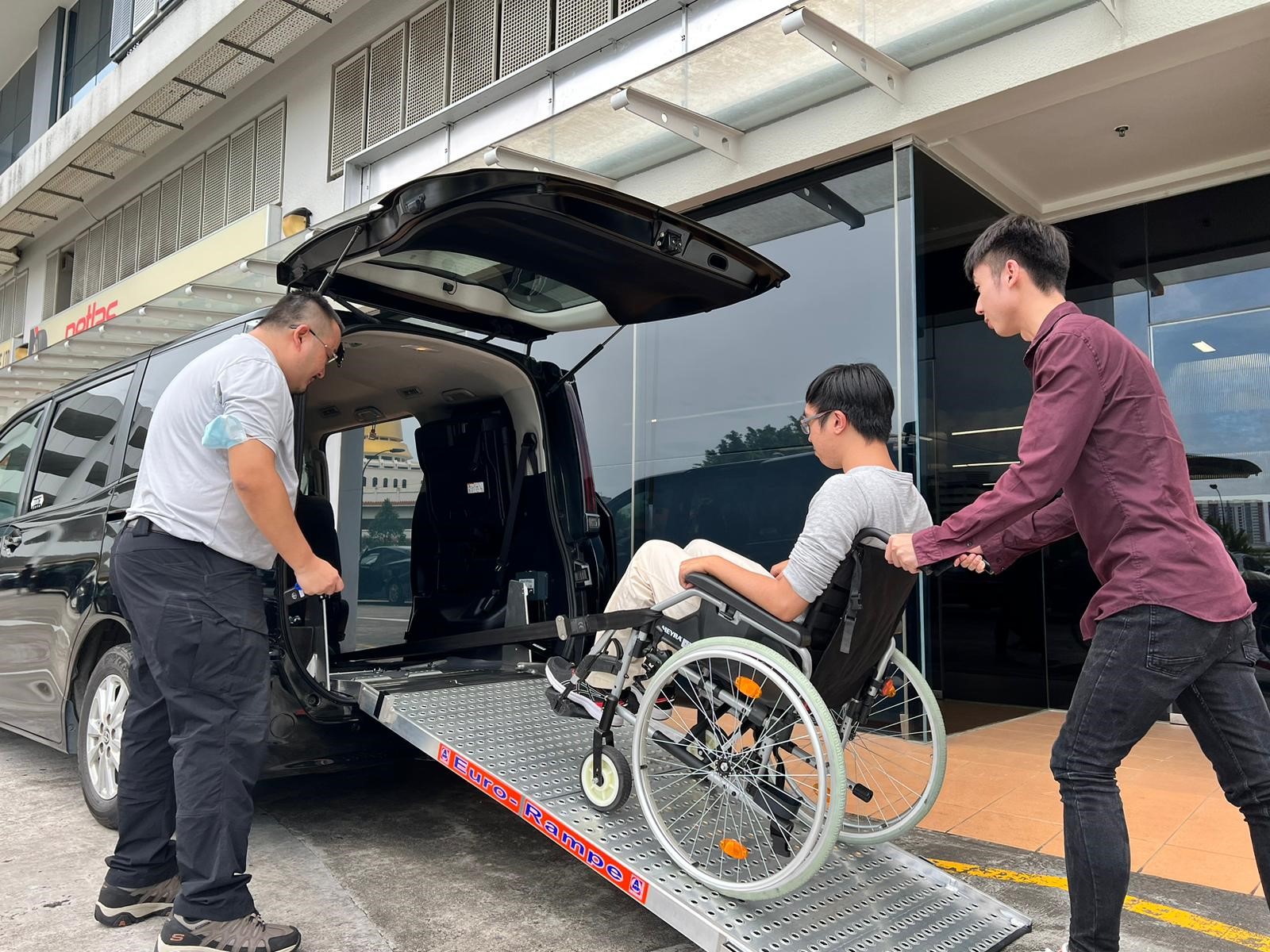 2 men helping a wheelchair user up a ramp of a black mini van